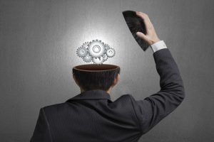 Working metal gears inside businessman head in gray concrete wall background