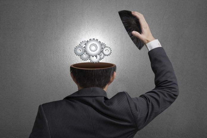 Working metal gears inside businessman head in gray concrete wall background